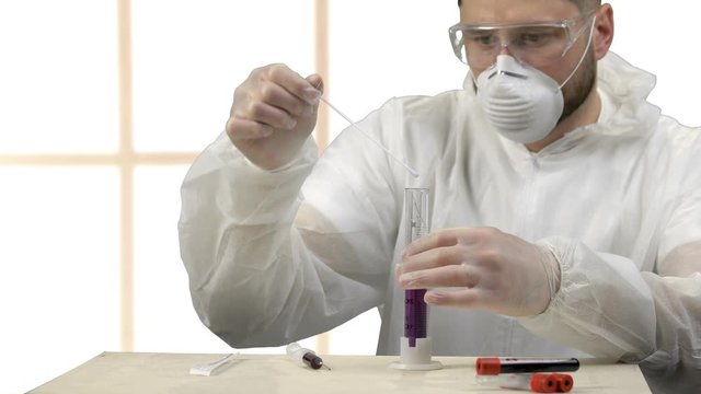 Medical scientist stirring up purple liquid in a test tube. Hardworking discovering antivirus medicine indoors. Windows on background.