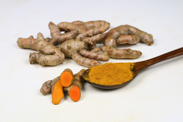 Turmeric powder in a wooden spoon and fresh turmeric roots isolated on a white background is an ingredient in turmeric foods and ingredients in skin care products. Turmeric helps the skin to be strong