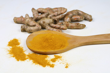 Turmeric powder in a wooden spoon and fresh turmeric roots isolated on a white background is an ingredient in turmeric foods and ingredients in skin care products. Turmeric helps the skin to be strong