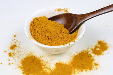 Turmeric powder in a wooden spoon and isolated white cup on a white background Used as an ingredient in skin care and food products. Turmeric helps the skin to be strong.