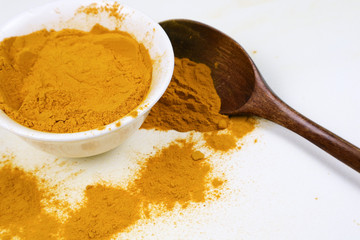 Turmeric powder in a wooden spoon and isolated white cup on a white background Used as an ingredient in skin care and food products. Turmeric helps the skin to be strong.