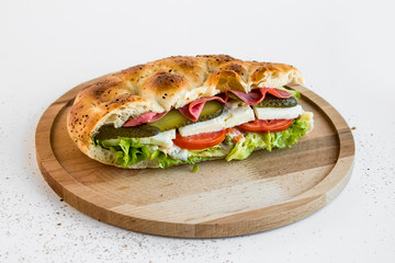 A big sandwich made with lettuce,white cheese,tomato,salami and cucumber pickle slices in bread pide of Ramadan on the round wooden tray.