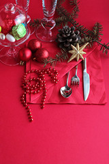 Traditional Christmas or New Year Table setting with luxury red napkin,cutlery set,red bead chain,chocolate and pine cone on the red surface.