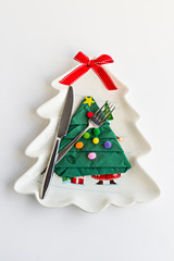 Porcelain plate in the shape of Christmas tree with cutlery set and napkin on white surface with copy space.