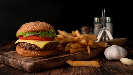 Close up view of Fresh tasty beef burger and french fries on wooden tray with seasoning and garlic
