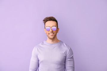 Young man with stylish sunglasses on color background