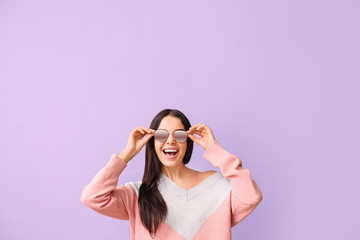 Young woman with stylish sunglasses on color background