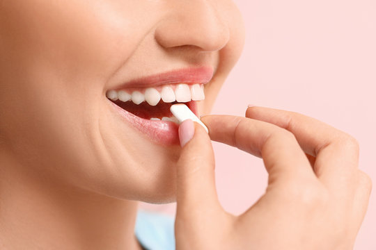Young woman with chewing gum on color background, closeup