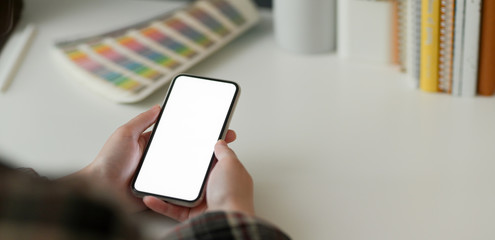 Cropped shot of female designer using mock-up smartphone while working with designer supplies