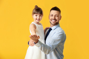 Father and his little daughter dancing against color background