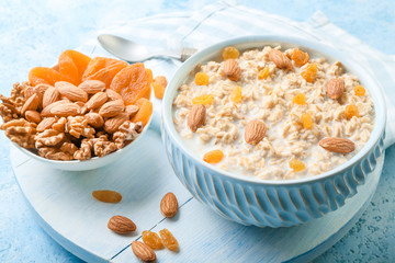 Fototapeta na wymiar Bowls with tasty sweet oatmeal, dry apricot and nuts on color background