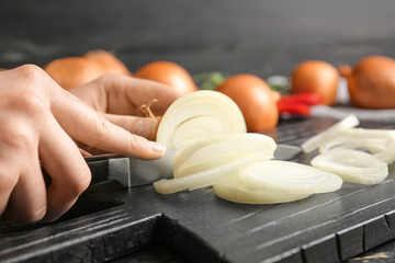 Woman cutting fresh raw onion on table, closeup