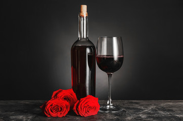 Bottle of wine, glass and roses on table against dark background