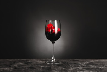 Glass of wine with rose petals on table against dark background
