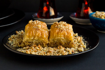 Traditional Turkish Pastry Dessert;Walnut Baklava on the stylish, black plate with diced walnuts and tea.