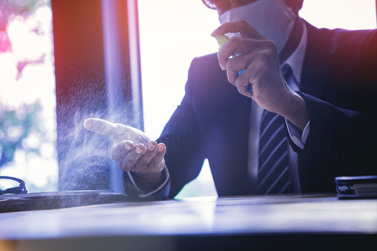 Businessman with mask applying alcohol spray for cleaning and protecting hands from virus disease