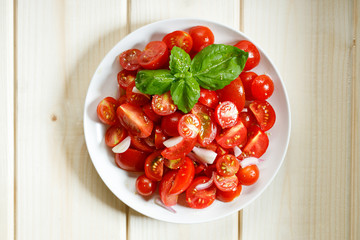 red cherry tomato and basil leaf on white plate on wooden background
