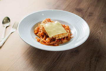 Pasta, Italian food, with tomato sauce topping with deep fried crispy pork cutlet and a sheet of cheese in white dish place on dark brown wooden table