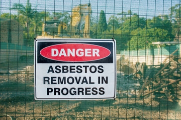 A warning sign Danger Asbestos on a fence at construction site where old house is demolishing