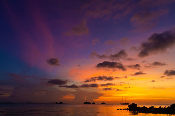 Colorful sunset on a tropical beach. Orange sunset on the ocean. Colorful sunset in the tropics. In the water is a sailing ship. Silhouetted sailboat with masts