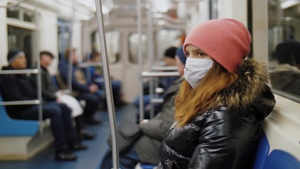 Young woman wearing medical face mask rides in subway. Protection against infection coronavirus covid-19 in public transport - Powered by Adobe