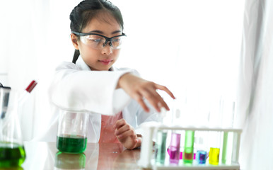 Asian cute little girl student child learning research and doing a chemical experiment while making analyzing and mixing liquid in glass at science class on the table.Education and science concept