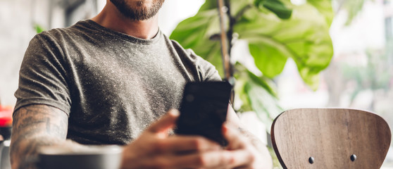 Handsome hipster man relaxing using digital smartphone with coffee and looking at screen typing message at table in cafe and restaurant,playing game online and social media