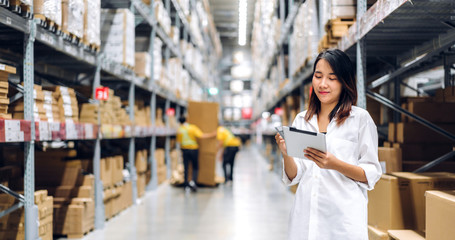 Portrait of smiling asian manager worker woman standing and order details on tablet computer for checking goods and supplies on shelves with goods background in warehouse.logistic and business export