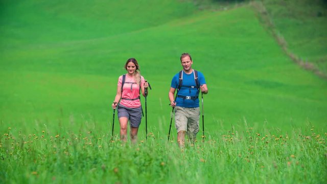 Clip of a couple that walk across a mountain meadow during an excursion. Trekking nordic walking video shot in Topla Valley, Crna na Koroskem, Slovenia