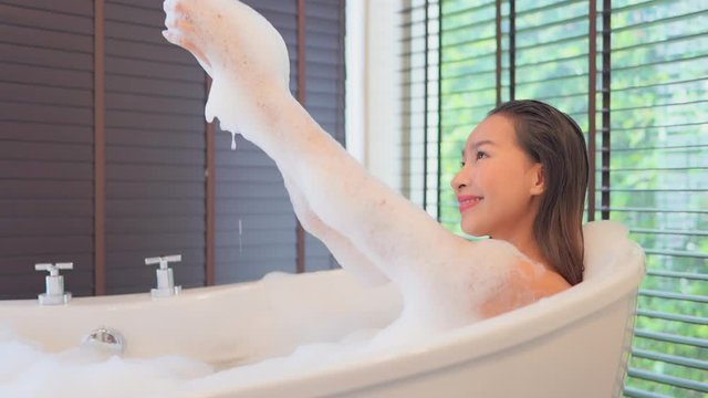 Close-up of a young healthy Asian woman taking a relaxing bubble bath while playing and washing with the bubbles. 