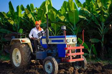 Indian / Asian farmer with tractor preparing land for sowing with cultivator, An Indian farming scene.