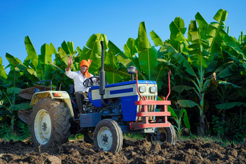 Indian / Asian farmer with tractor preparing land for sowing with cultivator, An Indian farming...