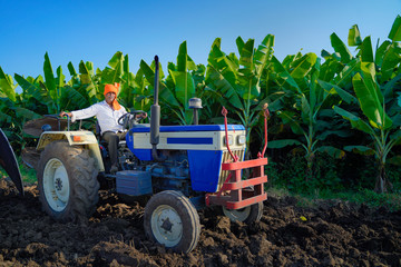 Indian / Asian farmer with tractor preparing land for sowing with cultivator, An Indian farming...