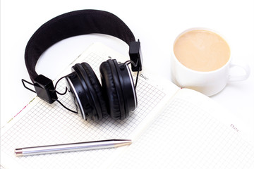 black headphones with a cup of coffee on a white background. notebook with pen on the table