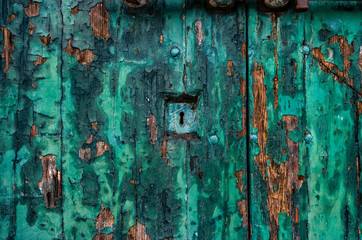 An old venetian door with keyhole. A wooden texture appears through the green paint.