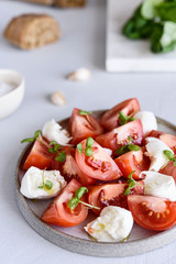 Italian Сaprese salad with sliced tomatoes, mozzarella cheese, basil, olive oil in a plate on grey concrete table. Selective focus