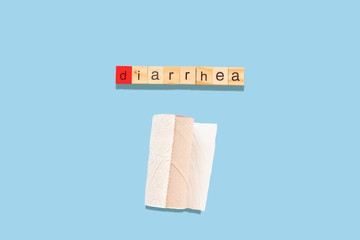 the word diarrhea made with wooden tiles on a blue background D is red and toilet paper under the...
