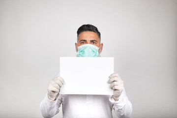 Portrait of man in surgical mask holding a white sign on white background.