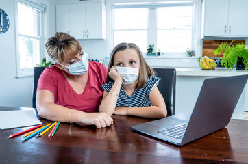 Coronavirus school closures and lockdown. Mum and bored daughter with masks studying online at home