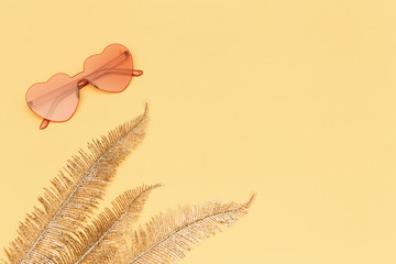 Flat lay with fashion glasses pink colored and golden palm leaves on yellow paper. Heart shaped eyeglasses. Trendly summer background with copy space.