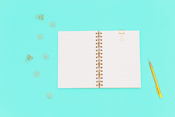 Top view of working table with open copybook on spring, yellow colored pencil,  golden metal clips for paper and documents. Flat lay with stationery for school, education.