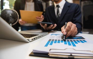 Business documents on office desk with tablet, graph and two colleagues discussing data working 