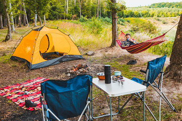 man laying on hammock at lake beach near camp fire