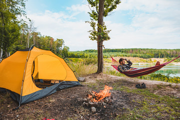 man laying on hammock at lake beach near camp fire