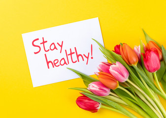 colorful tulips on a yellow background with white paper and text stay healthy