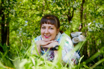 Portrait of an ugle fat chubby plump girl lying in grass and blossoming apple tree with white flower background in the park in a spring time