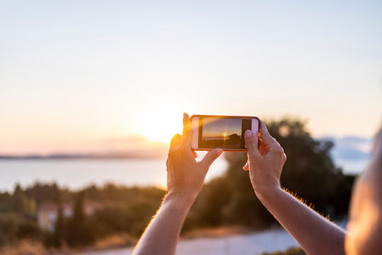 Woman taking a photo with her mobile phone at sunset