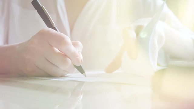Close-up. A woman signs a document and stamps. Slow motion. Sun flare. A woman is writing a pen.