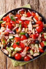 Summer salad with tuna, vegetables, olives and beans close-up in a plate on the table. Vertical top view