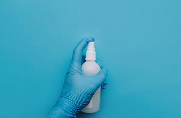 A hand in a blue medical protective glove holds a white bottle of pollinator on a clear blue background